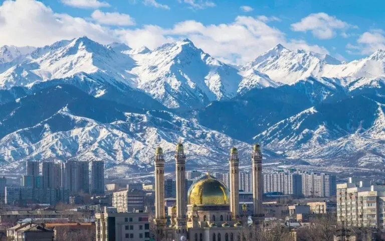 Almaty city skyline with a gold-domed mosque backed by the snowy Zailiysky Alatau mountains