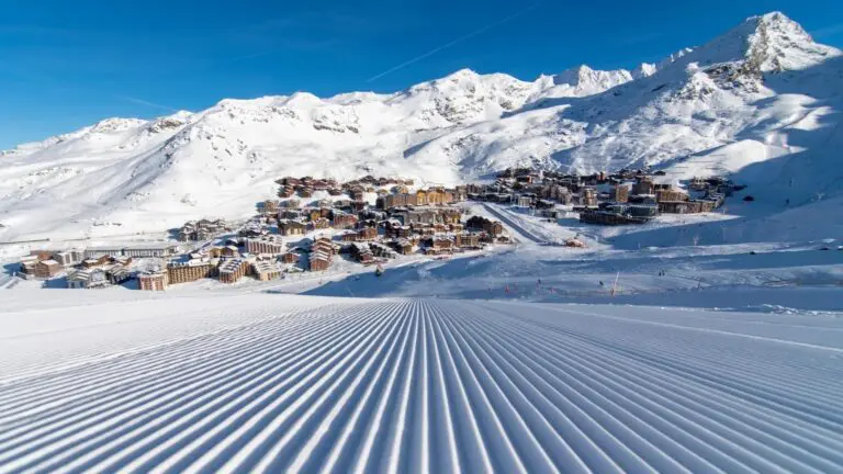 Freshly groomed piste in the foreground leading up to the village of Val Thorens under a clear blue sky